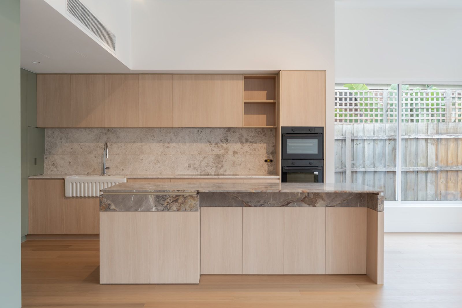 Glen Huntly kitchen: pale timber joinery, a stone-topped island and a high ceiling opening to the garden