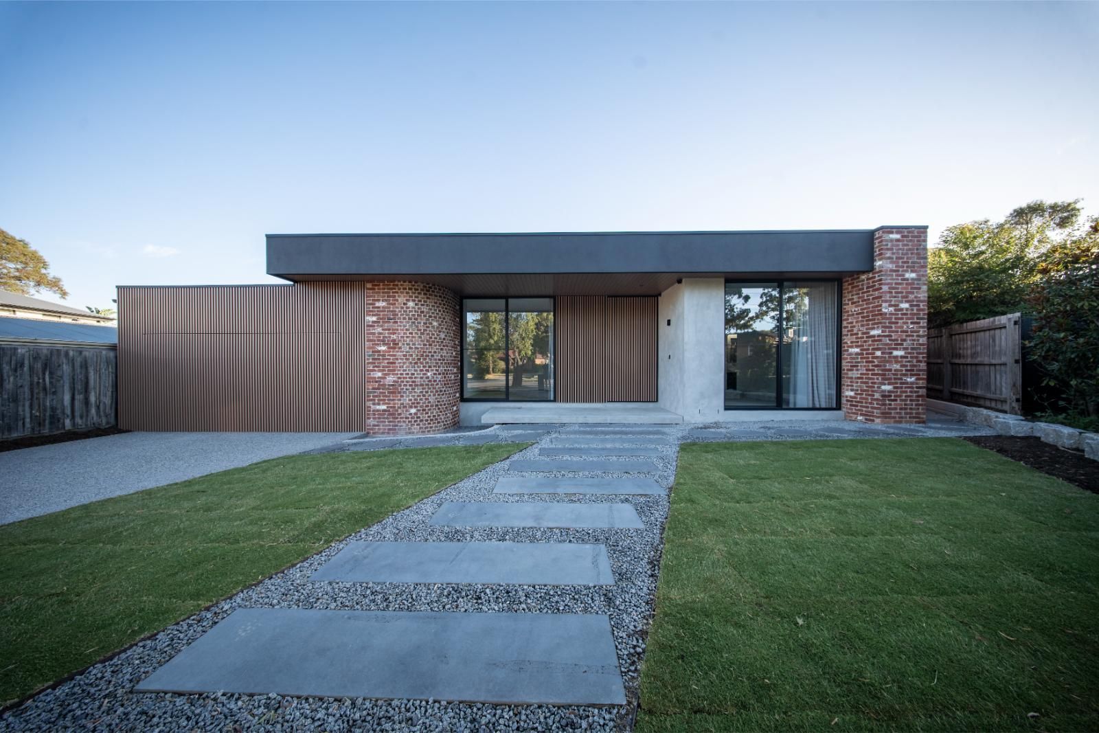 Front of the Wheelers Hill home: recycled red brick, timber cladding and a dark roofline behind a stepping-stone path across the lawn
