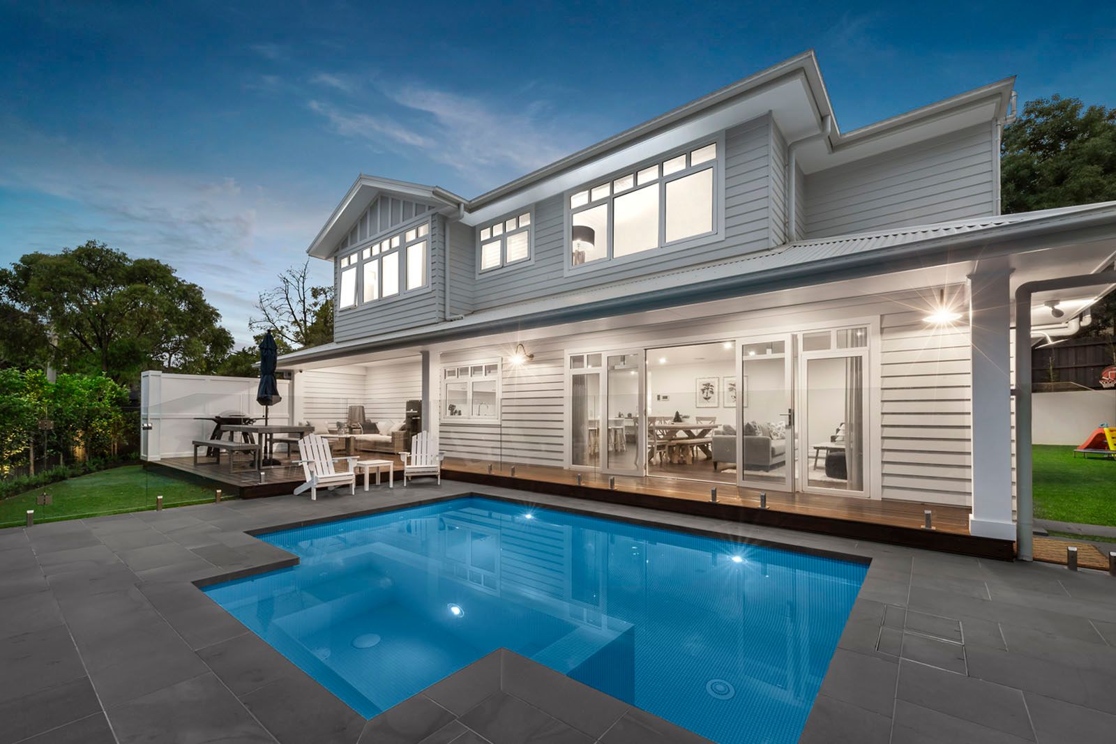Mitcham on Nara at dusk: a two-storey Hamptons-style home lit up behind the pool and deck
