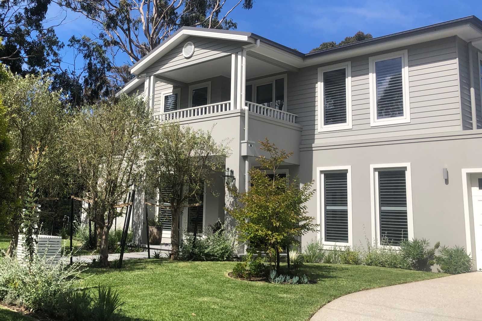 Somers home: a two-storey weatherboard house with a balcony, set behind a green lawn and established gums